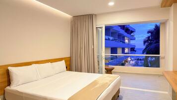 Une chambre d’hôtel avec un lit, une petite table et un balcon donnant sur la piscine et les bâtiments environnants.