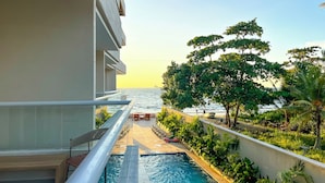Un espace piscine offrant une vue sur la mer, entouré de verdure et d’un bâtiment.