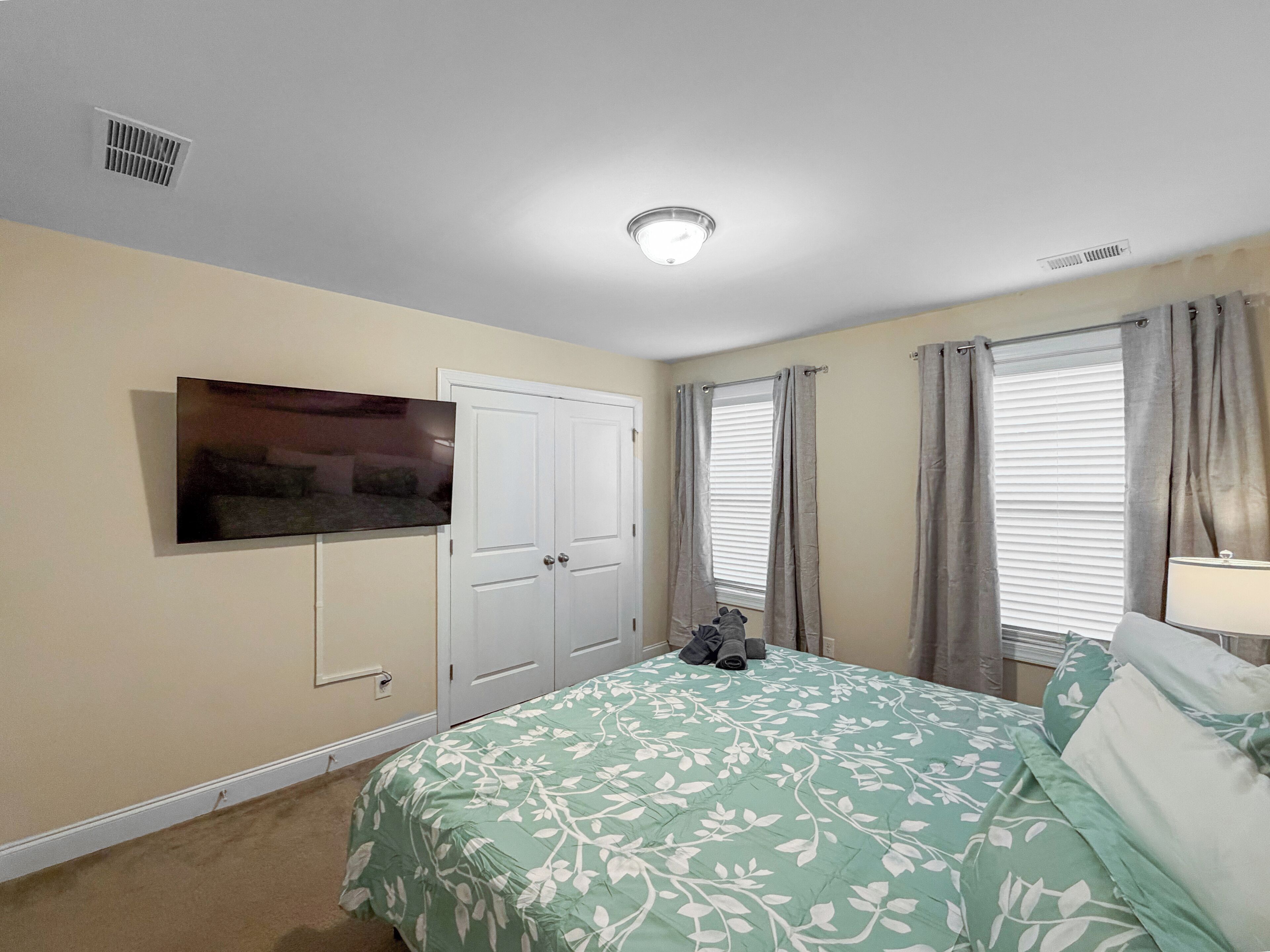 A bedroom with a bed, a TV mounted on the wall, a wardrobe, and a window with curtains.