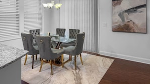 A dining area with a glass table surrounded by four grey upholstered chairs with gold accents. - 3 King Bdrs - Modern Fully Equipped Upscale House (Charlotte)