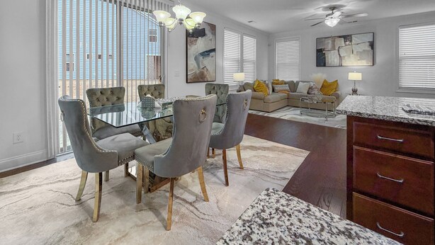 A modern kitchen with a dining area, featuring a glass-top table, grey upholstered chairs, and a ceiling fan. - 3 King Bdrs - Modern Fully Equipped Upscale House (Charlotte)