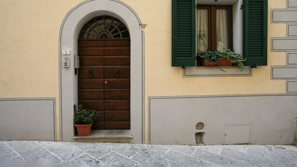A building with a wooden door, green shutters, and a potted plant. - Il Terrazzino (Cetona)