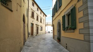 A narrow street with buildings on either side, featuring stone paving and green shutters. - Il Terrazzino (Cetona)