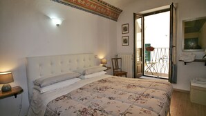A bedroom with a large bed, a nightstand with a lamp, a chair, and a view of the outside balcony. - Il Terrazzino (Cetona)