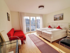 Een hotelkamer met een bed, een rode bank, een glazen tafel en uitzicht op gebouwen door het raam.
