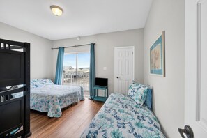 Ein Zimmer mit zwei Betten, einem Fernseher, einer Tür und einem Fenster mit Vorhängen.