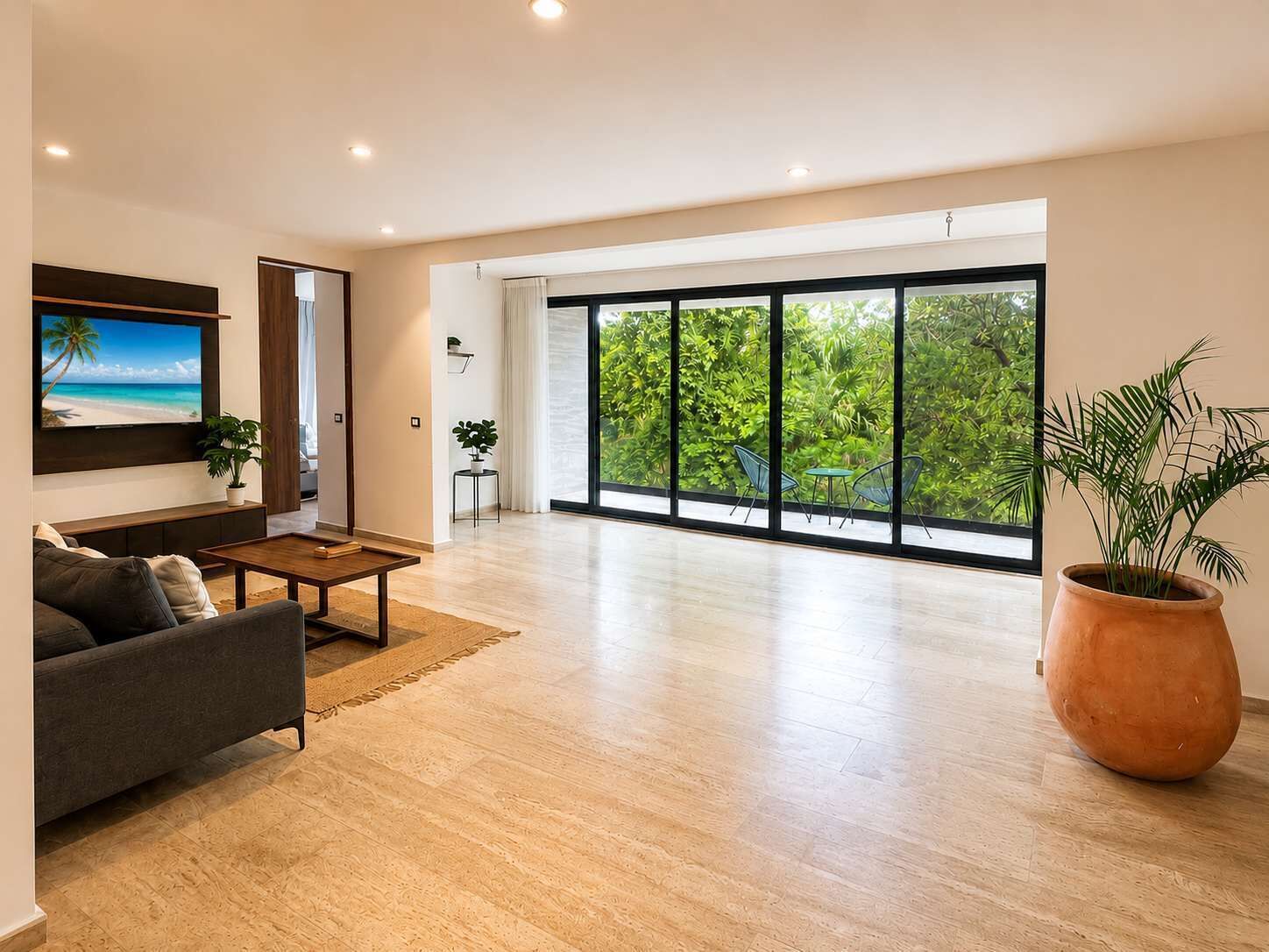 A spacious living room with a large window, a flat-screen TV, a sofa, a coffee table, and a potted plant.