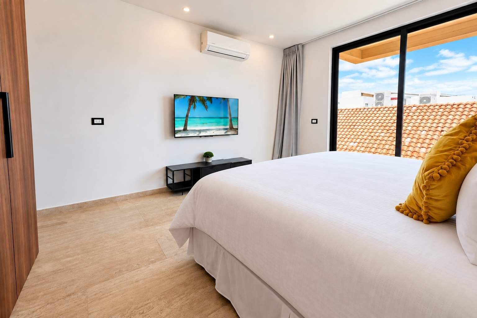 Un dormitorio con una cama grande, un televisor en la pared y un ventanal con vistas a edificios.