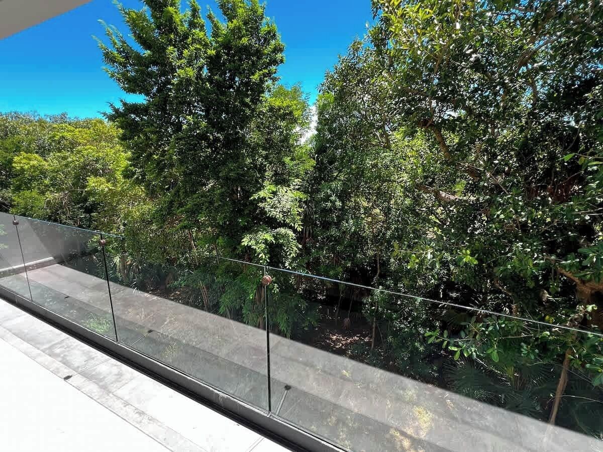 Un balcon doté d’une balustrade en verre, offrant une vue sur une forêt dense et verdoyante.