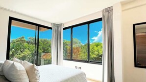Un dormitorio con una cama grande, dos ventanas con cortinas y vistas a la vegetación.
