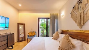 A hotel room with a large bed, a wooden headboard, a television on the wall, a desk with a chair, and a view of the outdoors through a glass door. - Ground Floor Condo with Marina View & Pool Access (Puerto Aventuras)
