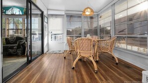 Een zonnige kamer met een houten vloer, een glazen deur, rieten stoelen en een hanglamp.