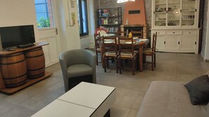 Una sala de estar con televisión, barriles de madera, un sofá, una mesa de comedor con sillas y una chimenea.