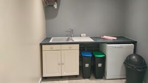 Una cocina compacta con un lavamanos, armarios, lavavajillas y contenedores de basura.