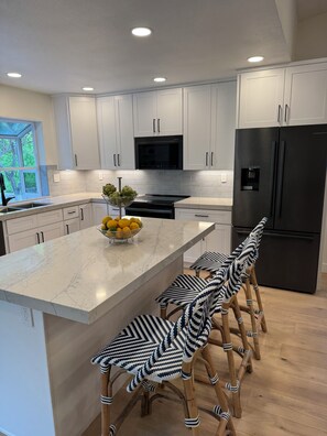A modern kitchen with white cabinets, a black refrigerator, a marble island, and a window with a view of greenery. - Comfortable San Diego Getaway 3BR Condo in Peaceful 55+ Community (San Diego)