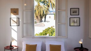 Una habitación con una cama, dos mesitas de noche, una ventana con contraventanas abiertas y cuadros en las paredes.