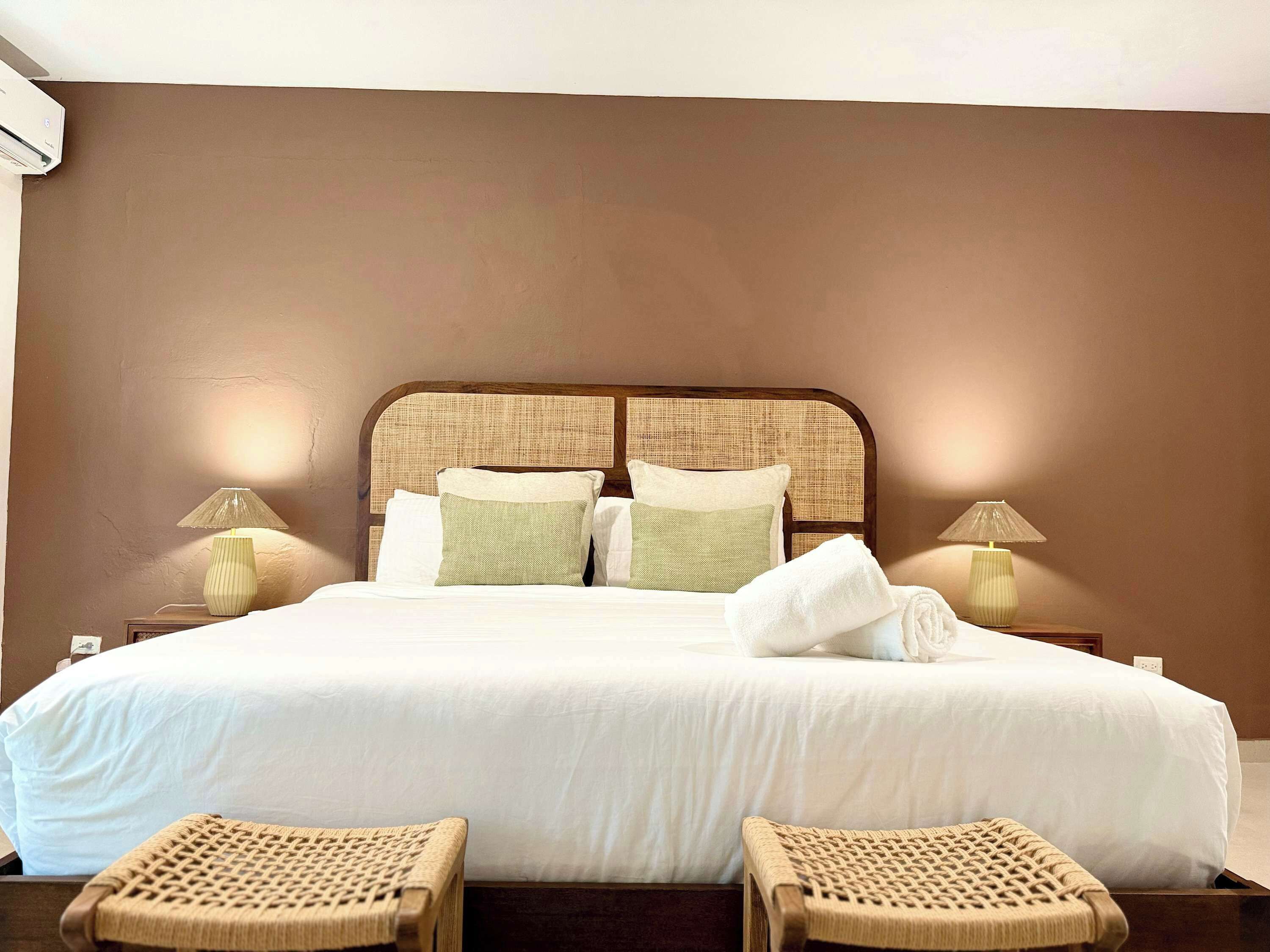 Ein Hotelzimmer mit einem großen Bett, zwei Nachttischlampen, einem Kopfteil und zwei Korbstühlen.