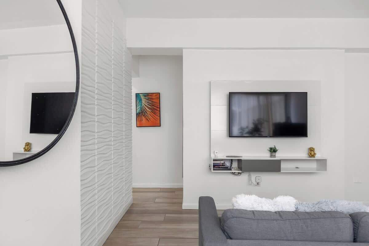 A modern living room with a grey sofa, a mounted TV, and a white textured wall.