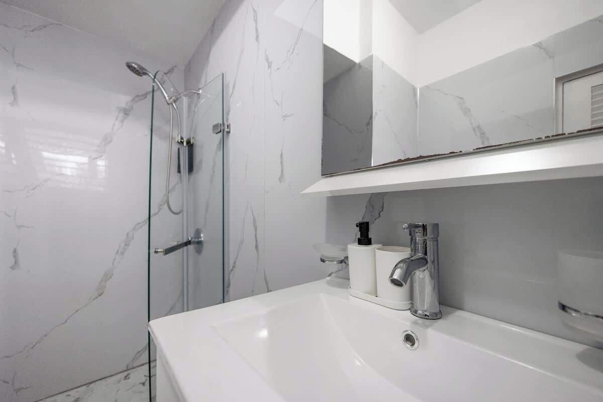 A modern bathroom with a white marble wall, a glass-enclosed shower, and a white sink with a mirror above it.