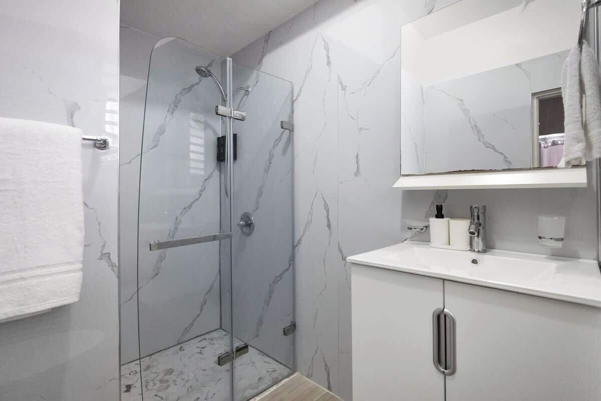 A modern bathroom with a glass shower enclosure, marble walls, and a white vanity with a mirror.