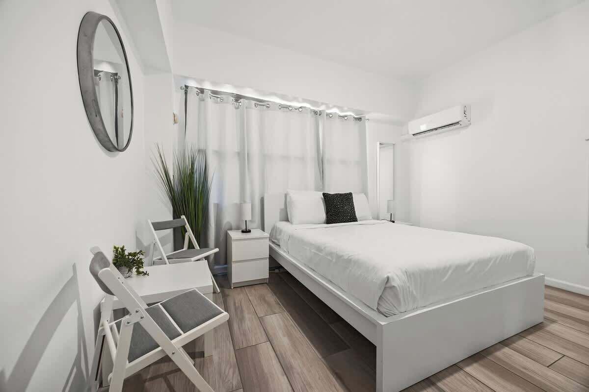 Une chambre moderne avec un lit blanc, des tables de chevet, un bureau et un miroir.