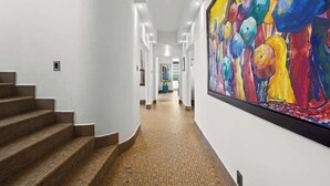 Un pasillo con una escalera a la izquierda y un cuadro grande y colorido en la pared derecha.