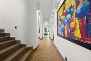 Ein Flur mit Treppe links und einem großen, farbenfrohen Gemälde an der rechten Wand.
