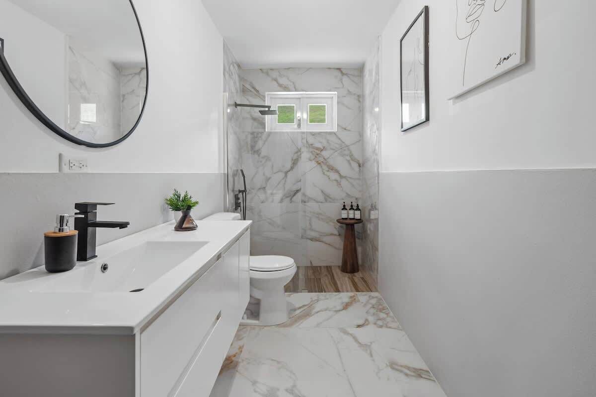 A modern bathroom with a white marble sink, a toilet, and a shower area.
