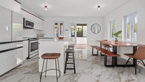 Una cocina moderna con armarios blancos, una isla central y un comedor con mesas y sillas de madera.