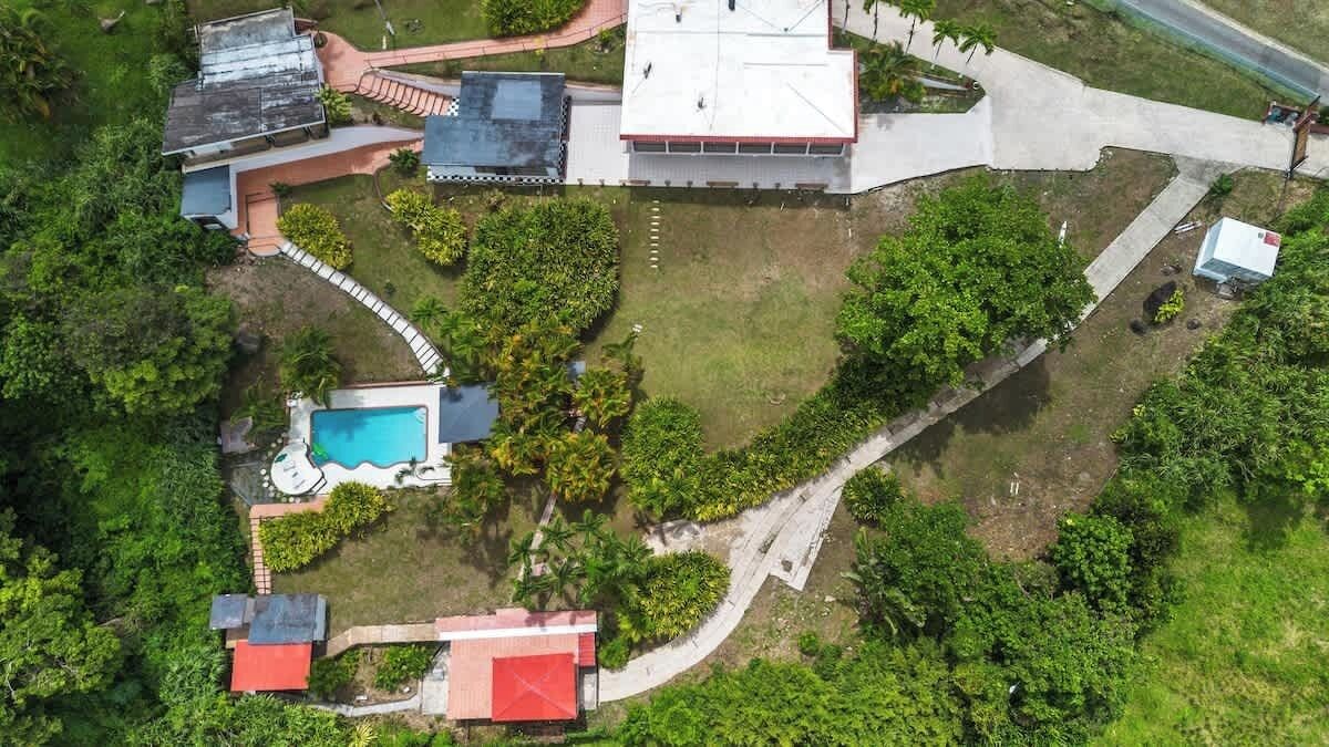 Una vista aerea di una proprietà residenziale con piscina, diversi edifici e vegetazione circostante.