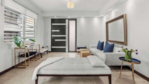 Uma sala de estar moderna com um sofá, uma mesa de centro, um banco e uma área de jantar com mesa e cadeiras.