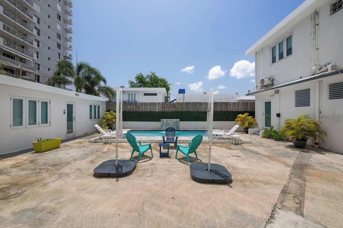 A rooftop pool area with a table and chairs, surrounded by potted plants and a view of a high-rise building.