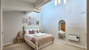 Ein Schlafzimmer mit Bett, Nachttischen, einem Spiegel und einer Heizung.