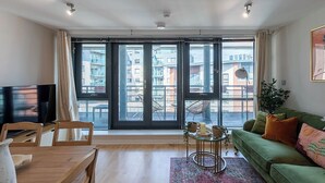 Ein modernes Wohnzimmer mit einem großen Schiebeglastür, die auf einen Balkon im Freien führt, einem grünen Sofa, einem Holzespeisetisch und einem Flachbildfernseher.