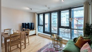 Ein modernes Wohnzimmer mit Essbereich, großen Fenstern und einem grünen Sofa.