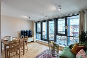Ein modernes Wohnzimmer mit Essbereich, großen Fenstern und einem grünen Sofa.