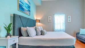 Een slaapkamer met een bed, nachtkastje, lamp en uitzicht door een raam.
