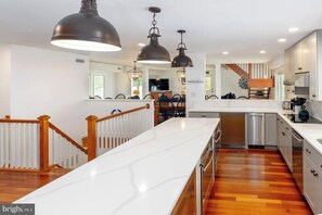 Una cocina moderna con encimeras blancas, suelo de madera e iluminación colgante.