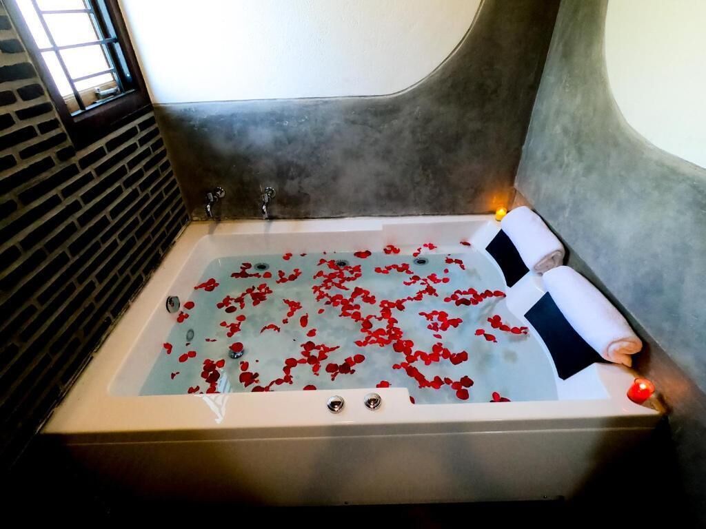 Eine mit Wasser und Rosenblüten gefüllte Badewanne, mit zwei Handtüchern und einer Kerze daneben.