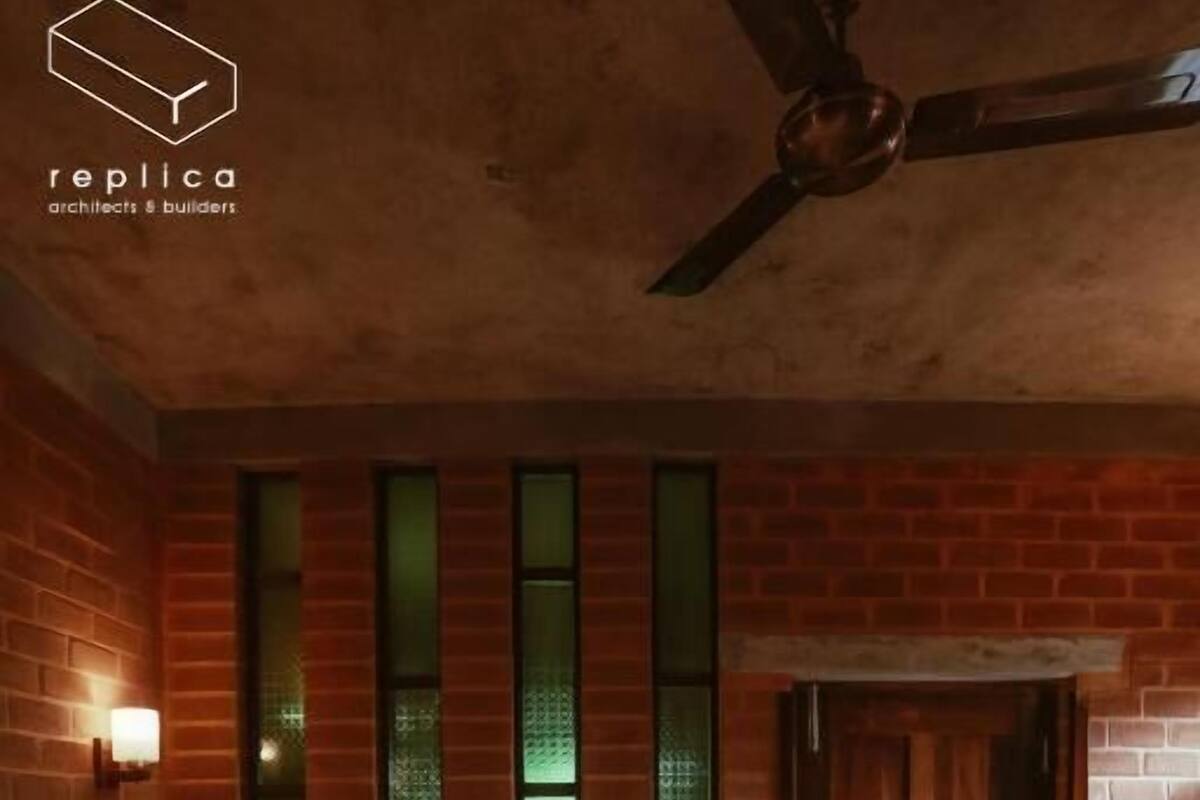 Une chambre d’hôtel avec un mur en briques, un lit avec du linge de maison blanc, une porte en bois et un ventilateur de plafond.