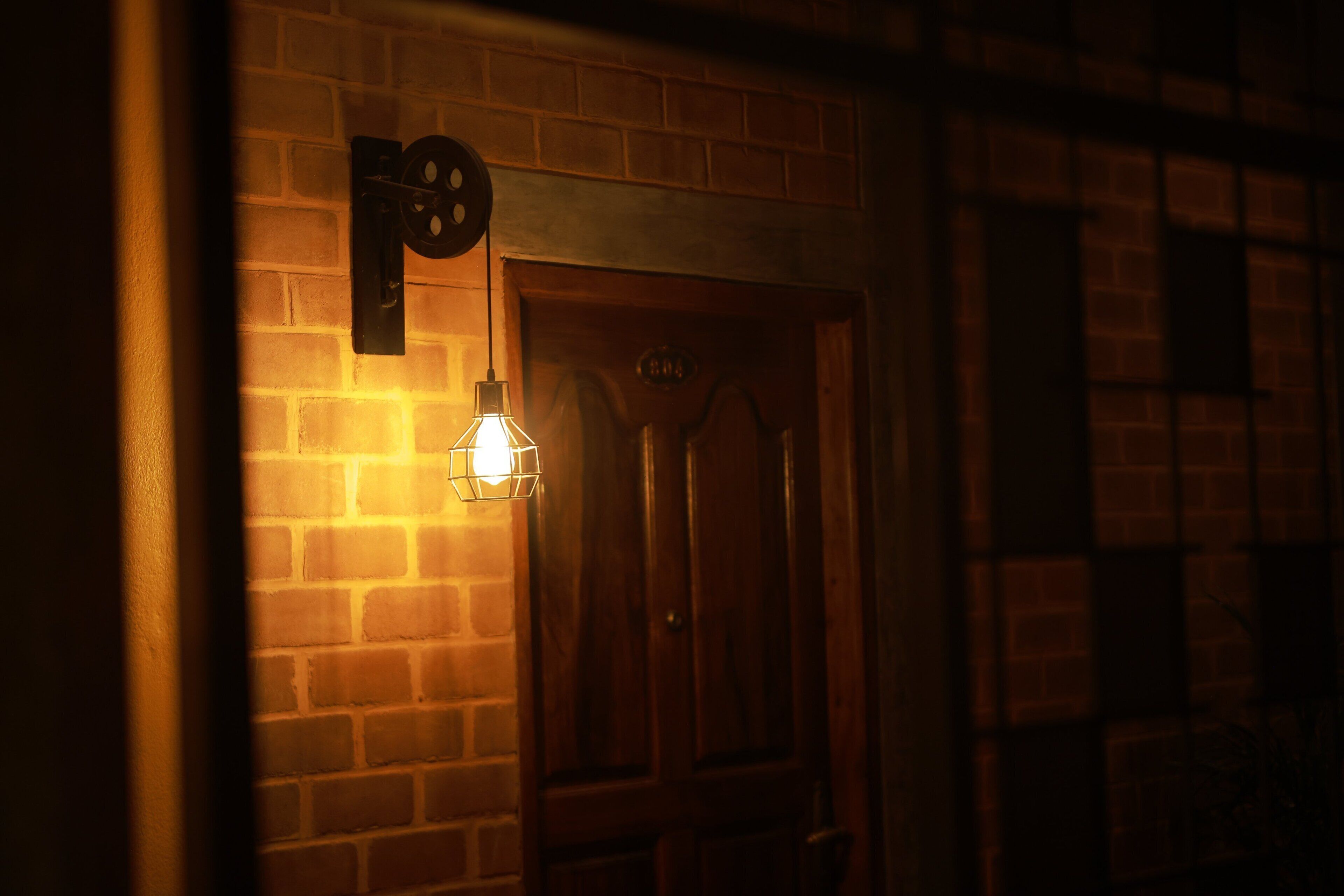 A brick wall with a wooden door and a wall-mounted light fixture.