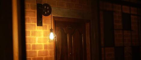 A brick wall with a wooden door and a wall-mounted light fixture.