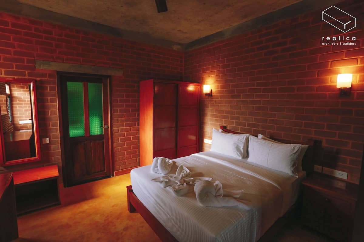 Une chambre d’hôtel avec un mur en briques, un lit avec du linge de maison blanc, une armoire en bois et un miroir.