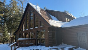 Eine Blockhütte mit einer großen Veranda und zahlreichen Fenstern, umgeben von verschneitem Gelände und Bäumen.