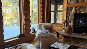 Ein gemütliches Blockhaus-Interieur mit Kamin, einer komfortablen Sitzecke und Blick auf den Wald.