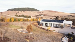 Una casa moderna con techo solar, rodeada por un jardín ajardinado con árboles y un paisaje montañoso al fondo.