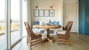 Comedor con sillas de mimbre, una mesa redonda y vistas amplias a través de grandes ventanales.