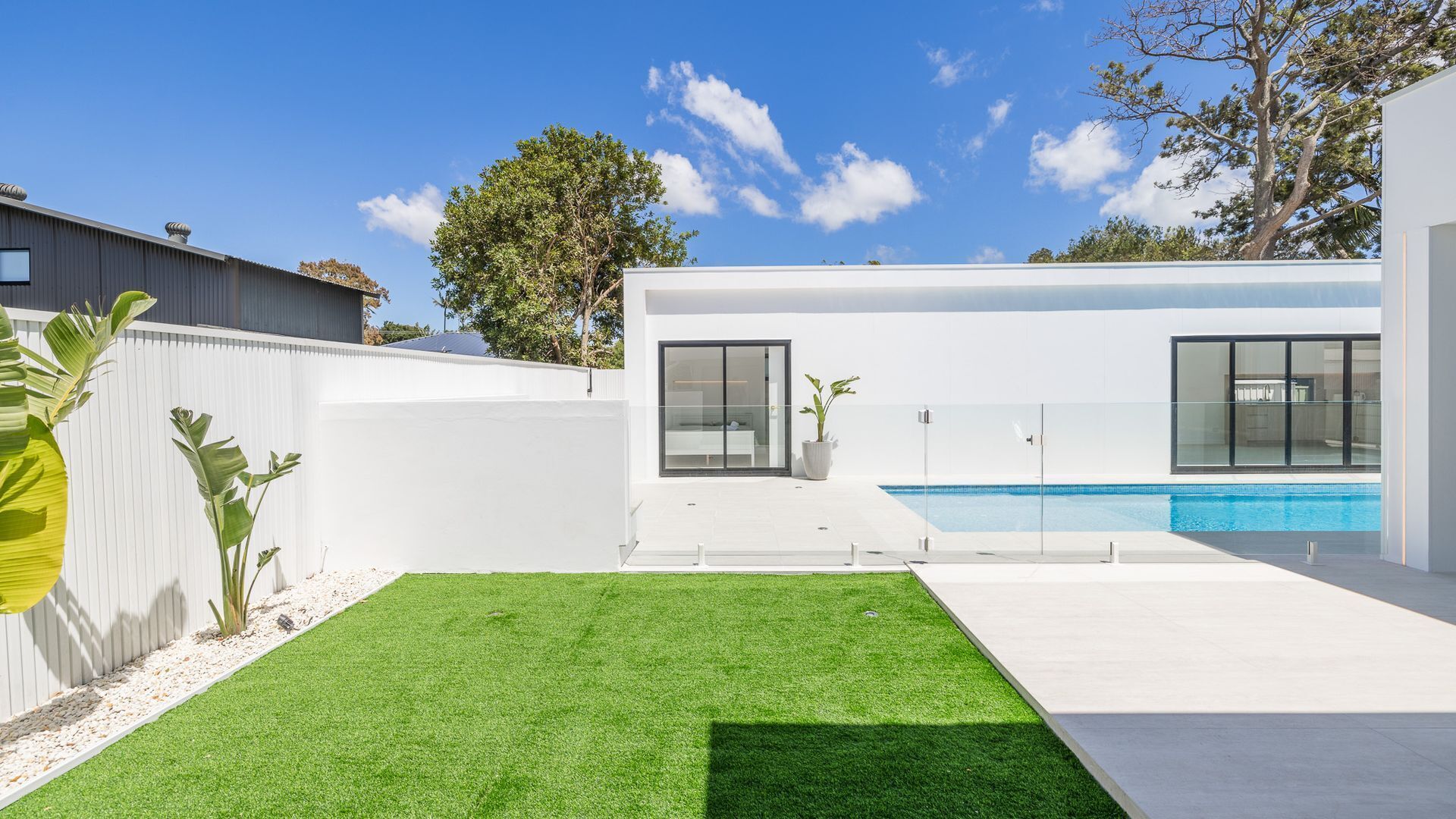 A modern house with a swimming pool, a well-maintained lawn, and a large tree in the background.