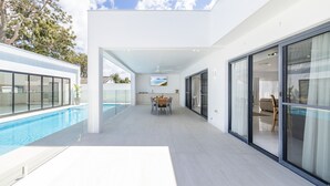 A modern house with a swimming pool, a dining area, and large glass doors leading to a balcony. - 57 Tomaree Road House - Pool, Air-con, Wi-fi, Boat Parking (Shoal Bay)
