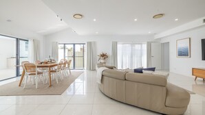 Un'ampia zona giorno con un divano beige capiente, un tavolo da pranzo con sedie e una cucina visibile attraverso una porta scorrevole in vetro.
